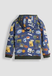 Kapuutisärk, mis on kaunistatud sinise kangaga ja värviliste telkimisega seotud plaastritega, sealhulgas loomade ja reisimise ikoonidega, ning rohelise soonikuga äärega.