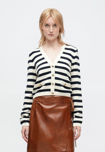 Cardigan rayé marine et crème avec un col en V, des boutons dorés et deux poches avant, associé à une jupe en cuir marron.
