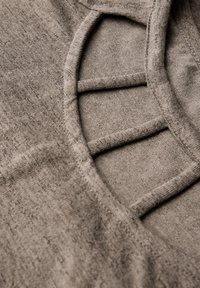 Světle hnědý pletený top s výstřihem ve tvaru lodě a horizontálními průstřihy. Měkká struktura s jemným, nepravidelným vzorem.