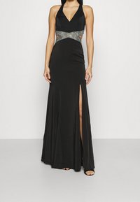 Černé maxi šaty na ramínka s v-výstřihem, které mají výřezy v pase a boční rozparek. Texturované kovové detaily v pase.