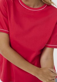 Red short-sleeve T-shirt with a round neckline and white piping along the collar and sleeves. Smooth fabric, loose fit, visible arm detail.