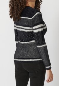 Stickad tröja i mörk marinblå med vita ränder och geometriska mönster. Mjuk textur, rund halsringning och figursydd silhuett.