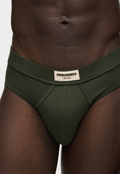 Slip vert foncé avec une étiquette beige portant la mention "DSQUARED2 MILANO", porté par une personne à la peau foncée avec un nombril visible.