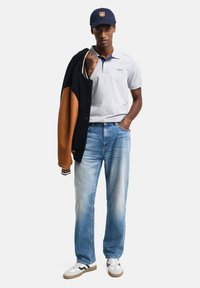 Grå polo skjorte med marine blå detaljer, svart og beige varsity-jakke, lyseblå jeans og hvite sneakers med svarte striper.