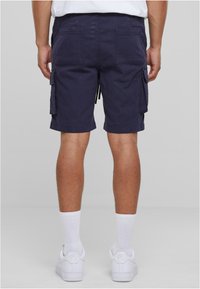 Marineblaue Cargoshorts mit zwei Gesäßtaschen und Seitentaschen, aus einem strapazierfähigen Stoff gefertigt, kombiniert mit weißen Sneakers und knöchellangen Socken.