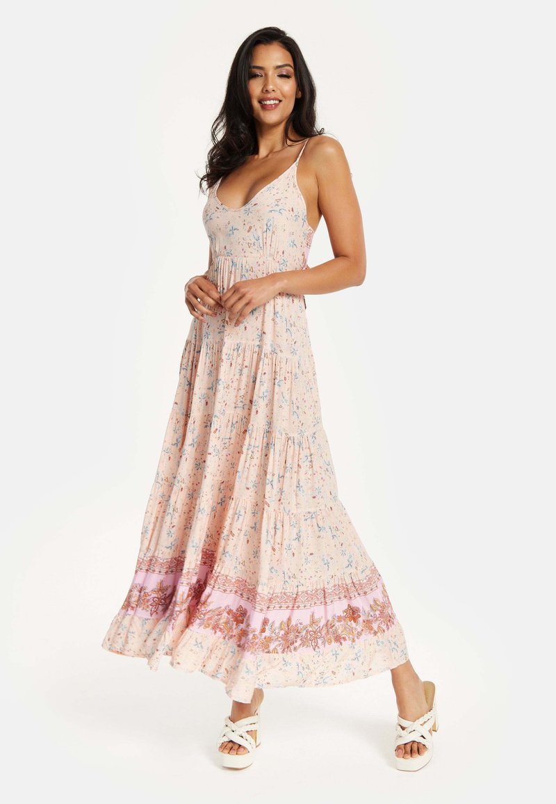 Maxi dress in light pink fabric with floral pattern, spaghetti straps, tiered design, contrasting band at hem with embroidery details.