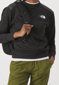 Felpa nera con collo tondo e logo, realizzata in tessuto liscio, abbinata a pantaloni verde oliva con vestibilità rilassata e tasche.