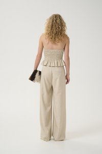 Haut beige à smocks avec détail peplum, associé à un pantalon beige à jambes larges. Le mannequin tient une pochette texturée avec un motif à pois.