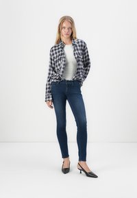 Kockás flanel ing sötétkék és fehér színben, szürke testhezálló felső, sötétkék skinny farmernadrág, fekete slingback magas sarkú cipő hegyes orral.
