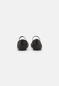 Zapatos de malla negros con suela plana, correas traseras y una superficie texturizada, que presentan un diseño básico y acentos de hardware mínimos.