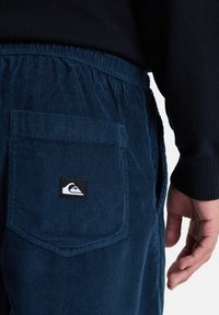 Marineblå kordfløypants med elastisk midjebånd og en baklommepå den bakre siden med en logopatch. Strukturert stoff og tapered design.