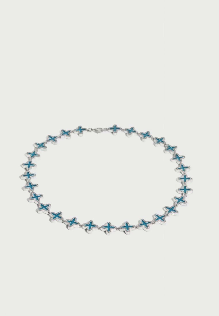 Un bracelet chaîne argenté orné de maillons répétés en forme de croix bleu turquoise, disposé en cercle sur un fond clair uni.