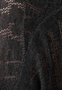 Svart stickad tyg med ett nätmönster, som har en mjuk textur och en lätt lyster. Viss variation i hålstorlekar genom materialet.