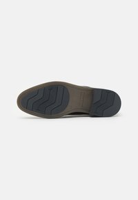 Suela de zapato con una base de goma marrón, patrón de tracción texturizado en negro y un branding sutil. La forma es ligeramente curvada con ranuras definidas.