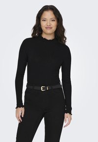 Svart ribbet langermet topp med høy hals og volangkant, kombinert med høyt liv svarte jeans og et tynn svart belte med gullspenne.