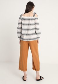 Off-shoulder randig blus i vitt och grått, med puffärm och knytband, som är ihop med ljusbruna vida byxor.