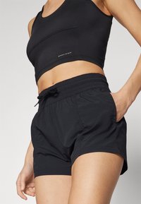 Pantalones cortos deportivos negros con cintura elástica y cordón ajustable, que cuentan con bolsillos laterales y una tela ligera y texturizada.