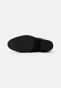 Suela de zapato de goma negra con un patrón texturizado que presenta surcos profundos y letras en relieve. Bordes suaves y diseño de tacón redondeado.