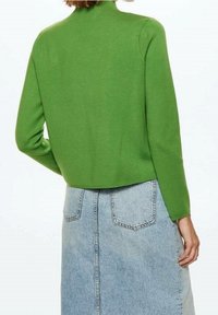 Pull vert en tricot avec un col montant, une coupe ajustée et des manches longues, associé à une jupe en denim clair avec des poches arrière.