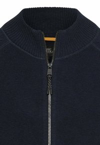 Donkerblauwe, gebreide trui met ritssluiting aan de voorkant, hoge kraag en gestructureerde stof. Voorzien van een contrasterende gele binnenvoering.