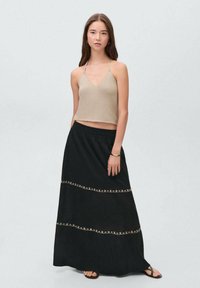 Beige cropped top with thin straps and v-neck, paired with a long black skirt featuring gold decorative stitching and an elastic waistband.