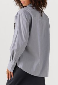 Gestreepte lange mouwen shirt met verticale blauwe en witte strepen, een hoge kraag en knoopmanchetten, gemaakt van lichtgewicht stof.
