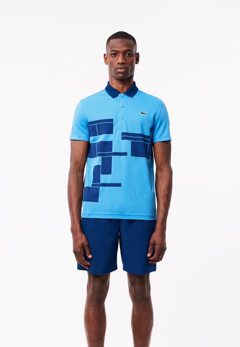 Polo bleu avec un col contrastant bleu marine, orné de motifs géométriques bleu marine. Porté avec un short bleu marine assorti.