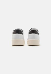 Hvite lær sneakers med en svart hælflik, rund form, teksturert overflate og beige gummisåle, med sømdetaljer.