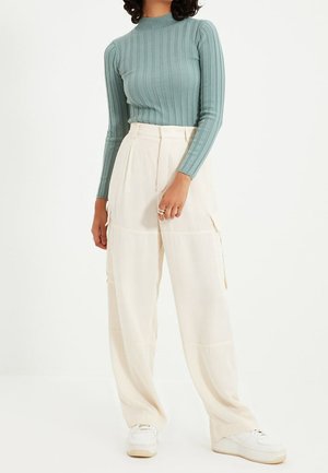 Un haut à manches longues côtelé bleu clair associé à un pantalon cargo large crème. Les baskets ont une tige blanche et une semelle claire.