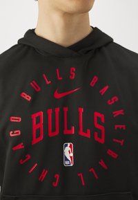 Person in einem schwarzen Hoodie mit roten "Chicago Bulls Basketball"-Schriftzug, Nike-Logo und NBA-Logo auf der Vorderseite.