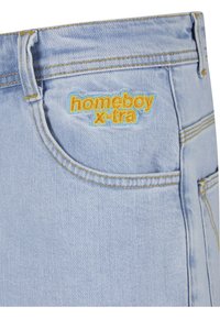Blugi din denim albastru deschis cu cusături galbene, un buzunar frontal și "homeboy x-tra" brodat deasupra buzunarului în galben și albastru.