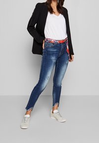 Blå denim skinny jeans med slitna detaljer och fransade benslut, tillsammans med en vit T-shirt och en svart blazer, toppat med ett färgglatt bälte.