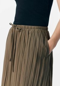 Falda plisada marrón con cinturilla elástica y detalle de cordón, combinada con una blusa negra ajustada. Tiene bolsillos laterales.