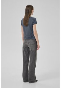 Graues, tailliertes T-Shirt mit kurzen Ärmeln, kombiniert mit hochgeschnittenen, weiten schwarzen Jeans, die subtile Nähte und Gesäßtaschen aufweisen.