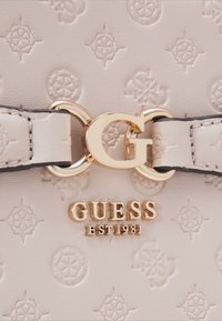 Borsa a tracolla beige chiaro con loghi in rilievo, hardware dorato e un evidente accento con la lettera "G". Presenta un design strutturato e una texture liscia.