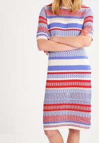 Neulemekko, jossa on vaakasuorat raidat punaisena, sinisenä ja kermanvärisenä. Lyhyet hihat ja suora malli, jossa on teksturoitu kuvio.