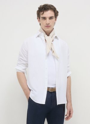 Camicia bianca di lino con bottoni indossata sopra una canottiera bianca, abbinata a jeans di denim blu scuro. Una sciarpa beige è annodata intorno al collo.