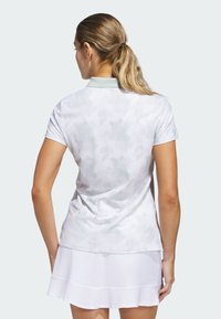Hvid polo shirt med et lys gråt camouflage mønster, korte ærmer, krave og et blødt, struktureret stof. Båret med en hvid nederdel.