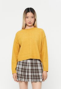 Sweter w musztardowym kolorze, wykonany na drutach, z okrągłym dekoltem, opuszczonymi ramionami i prążkowanym wykończeniem, połączony z plisowaną spódniczką mini w kratę.