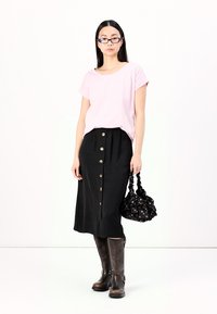 Top corto a maniche corte rosa chiaro, gonna nera con bottoni davanti, stivali marroni al ginocchio e una borsa a tracolla nera con un design arricciato.