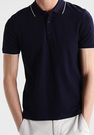 Marineblå polo med klassisk krave, to-knaps åbning og kontrasterende hvid kant ved kraven. Fremstillet af glat stof.