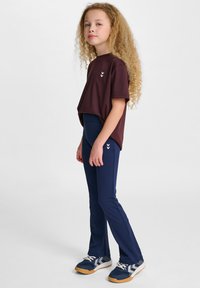 Mörkröd kortärmad t-shirt kombinerad med marinblå stretchbyxor, med en subtil logotyp. Barnet har på sig marinblå sneakers med grå detaljer.
