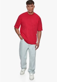 Camiseta roja de manga corta con un corte relajado, combinada con unos vaqueros de pierna ancha en azul claro y zapatillas blancas, que presentan una etiqueta de logo sutil.