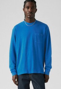 Long-sleeve blue cotton t-shirt with a crew neckline and a left chest pocket. Features ribbed cuffs and a relaxed fit.