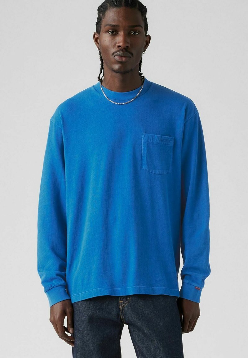 Long-sleeve blue cotton t-shirt with a crew neckline and a left chest pocket. Features ribbed cuffs and a relaxed fit.
