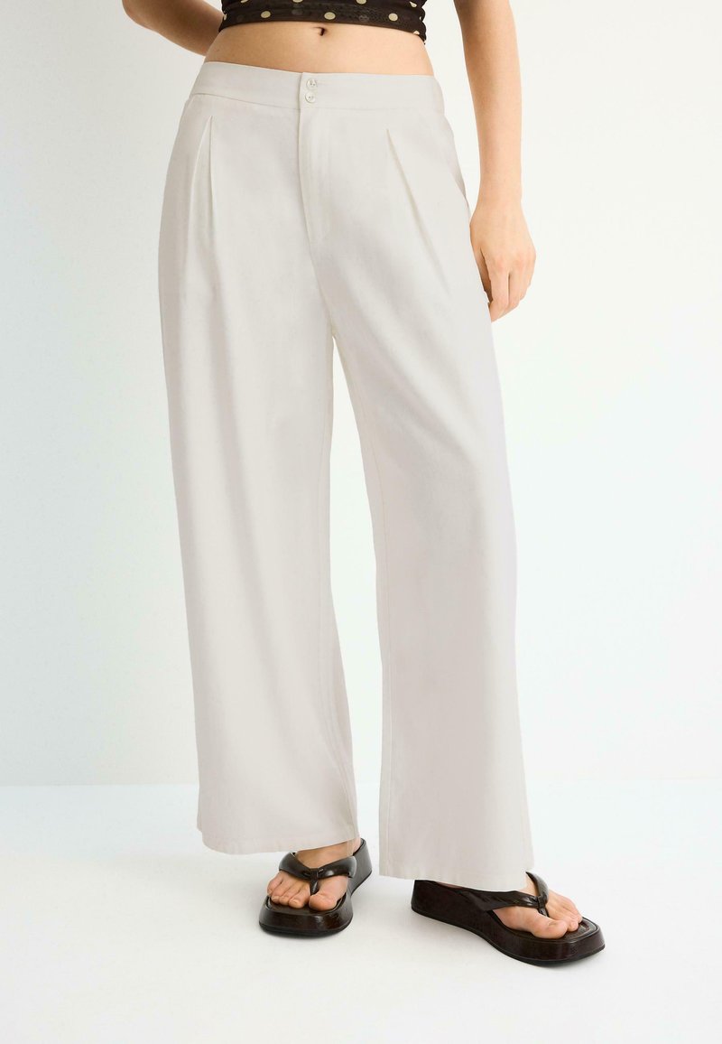 Pantalons blancs larges pour femmes avec boutons à l'avant, associés à des sandales noires à plateforme et lanières, vus de la taille aux pieds.