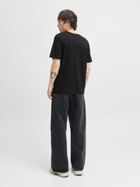 Mustapaitainen lyhythihainen t-paita, jossa on suora leikkaus. Yhdistetty väljiin tummiin farkkuihin ja vaaleisiin lenkkareihin. Minimiaalinen näkyvä kuvio.