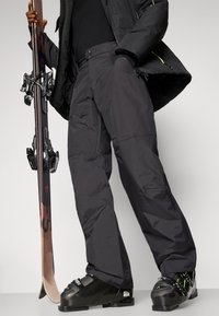 Calças de esqui pretas com um ajuste solto, feitas de material resistente à água, apresentando bolsos laterais e acabamentos costurados. Uma prancha de snowboard está segurada ao lado.