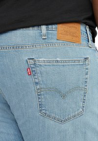Helle blaue Denim-Jeans mit einem Leder hinten angebrachten Patch und einem roten Logo-Tag. Sie verfügen über ein klassisches Fünf-Taschen-Design mit Kontrastnähten.