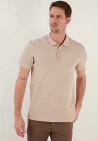 Béžová polo košile vyrobená z bavlněné směsi, s klasickým límečkem, dvouřadým knoflíkovým zapínáním a krátkými rukávy, s texturovaným vzhledem.